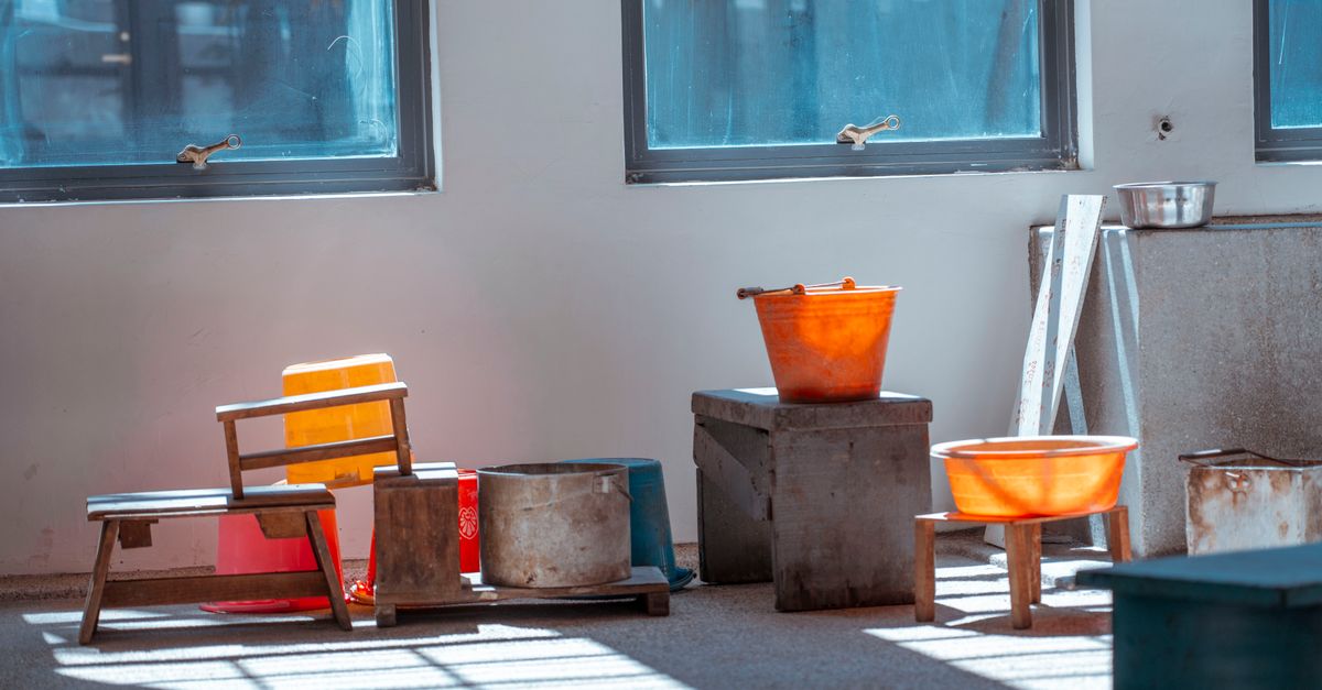 Artistic still life of wooden stools and plastic buckets in a rustic indoor setting.
