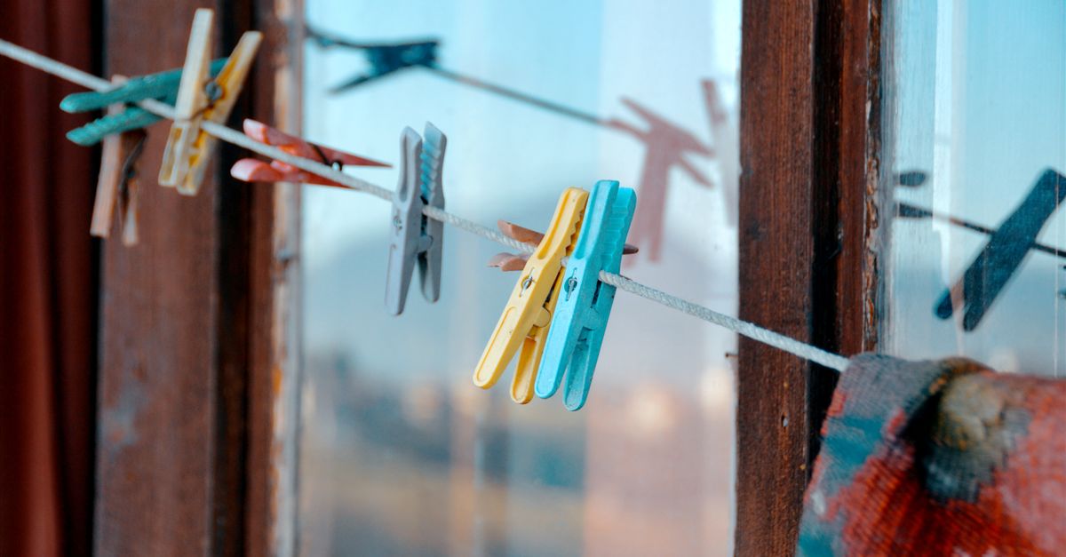 Vibrant clothespins hanging on a clothesline by a rustic window.